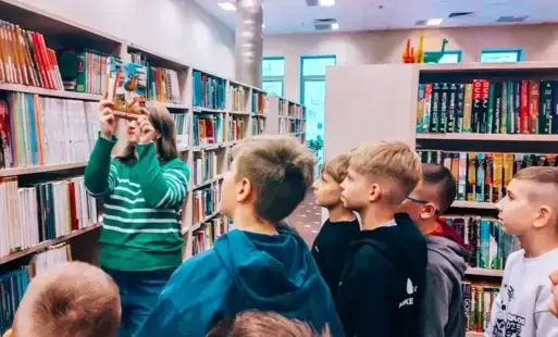 Bibliotekarka pokazuje dzieciom książkę z serii o Neli. 
