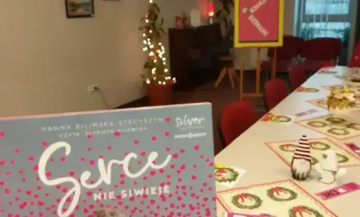 Tytułowa okładka książki pt. 'Serce nie siwieje' Hanny Bilińskiej-Stecyszyn. Okładka książki w kolorowej tematyce. Za książką widoczny fragment pomieszczenie wraz ze świątecznymi dekoracjami i przystrojonym stołem, w tle logo DKK.