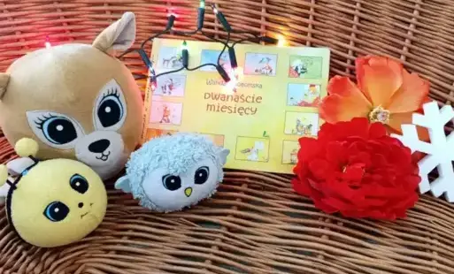ekspozycja książki, maskotek, sztucznych kwiatów i śnieżynki w wiklinowym koszu.