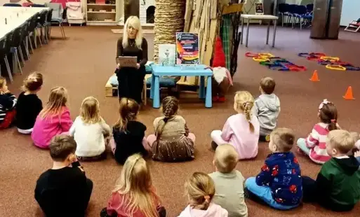 Tytułowe: Bibliotekarka czyta przedszkolakom zagadki podczas zajęć w Oddziale Dziecięcym.