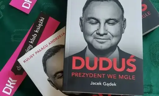 Na ciemno zielonej serwecie książka, fioletowe emblematy Dyskusyjnego Klubu Książki.