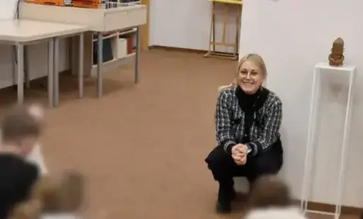 Uczniowie siedzą na kolorowych pufach przodem do bibliotekarki prowadzącej spotkanie. Prowadząca uśmiecha się.