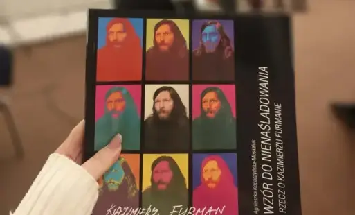 Na pierwszym planie książka „Wzór do nienaśladowania. Rzecz o Kazimierzu Furmanie” trzymana przez osobę niewidoczną na zdjęciu. W tle prowadząca Agnieszka Kopaczyńska-Moskaluk oraz goście spotkania