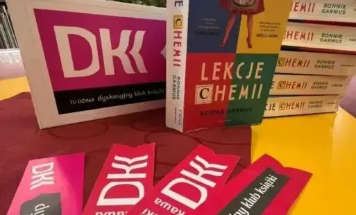 na pierwszym planie zakładki z napisem DKK, w tle książki i kwiaty