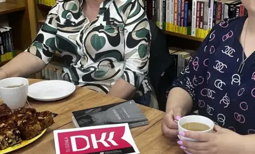Dwie osoby przy stole, między nimi filiżanki i logo DKK