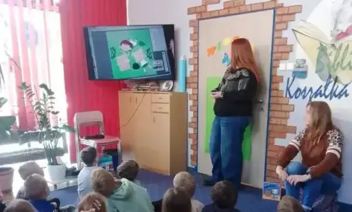 Dwie kobiety z grupą dzieci oglądają film edukacyjny na telewizorze
