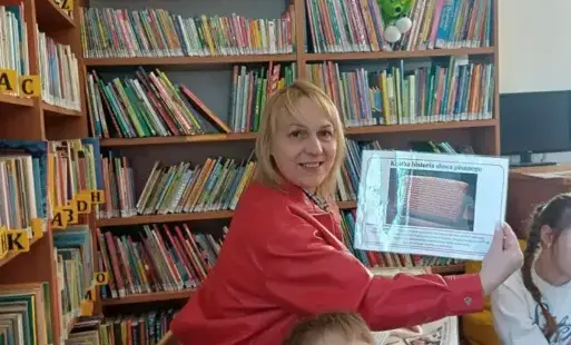 Kobieta prezentuje plansze na tle regałów z książkami.