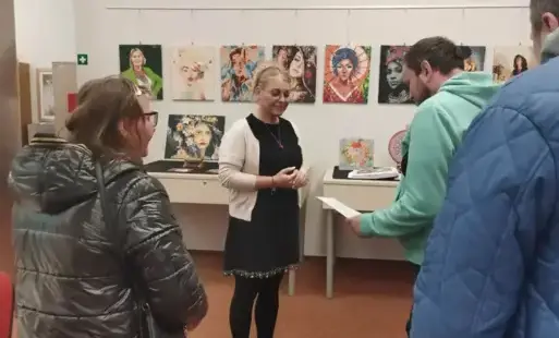 Na tle wystawy bibliotekarka przyjmuje kartkę z życzeniami od mężczyzny