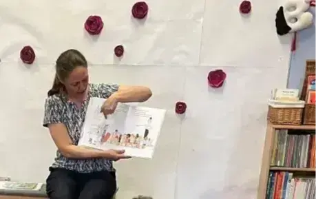 Zdjęcie startowe – Dzieci siedzą na kolorowej chuście, a prowadząca czyta im książkę i pokazuje ilustracje.