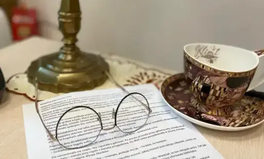 stół, a na nim lampka w dawnym stylu, filizanka, okulary oraz inne materiały pomocnicze.