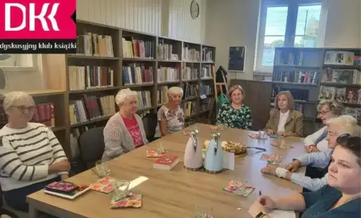 Fragment fotografii wraz z uczestnikami DKK, siedzącymi przy stole w bibliotece.
