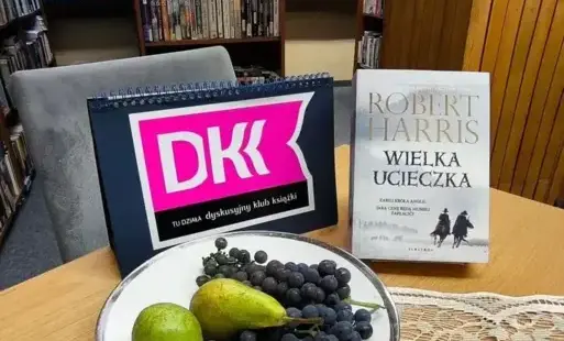 Okładka książki na stole obok owoce na talerzu i logo DKK