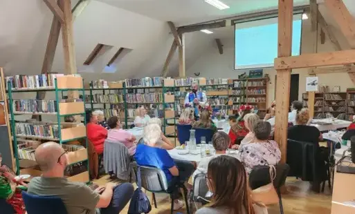 Grupa słuchaczy siedzi przy stołach, w głębi sali stoi prowadzący spotkanie mężczyzna.