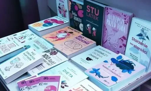 Wystawa książek prezentowana w Wypożyczalni Naukowej. Na stole znajdują się książki oraz ulotki informacyjne dotyczące Weekendu Seniora z Kulturą.  Publikacje są wyeksponowane w kilku rzędach, a obok nich umieszczono materiały promocyjne. 