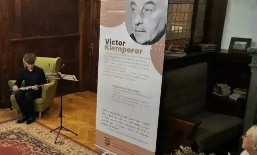 Na środku rollup ze zdjęciem i informacjami na temat Klepmerera. z lewej na fotel siedzi muzyk.