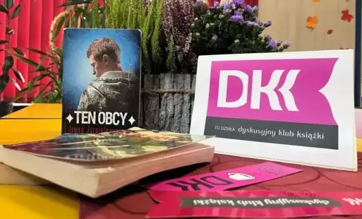 Na stole książki, zakładki DKK oraz duża donica z kwiatami.