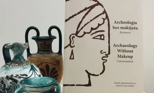 Książka „Archeologia bez makijażu” stoi na podstawce na stoliku, obok niej znajdują się trzy antyczne wazoniki