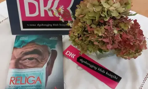 Na jasnej serwecie emblematy Dyskusyjnego Klubu Książki, książka oraz bukiet bordowo-zielonych hortensji.