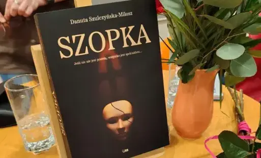 Umieszczona na małej sztaludze książka pt. Szopka. Na stoliku kwiaty.