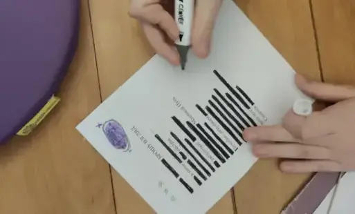 Zbliżenie na leżącą na podłodze kartkę z nowo utworzonym wierszem, nad nią ręka trzymająca flamaster