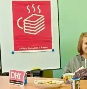 W tle plakat DKK, na stole logo DKK obok osoba z książką