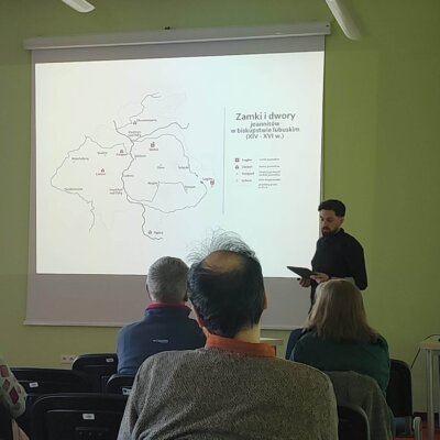 Krzysztof Wroński na tle slajdu z mapą. Kliknięcie powoduje powiększenie zdjęcia