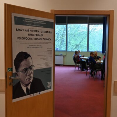 Plakat konferencji "Łączy nas literatura i historia. Hans Fallada po dwóch stronach granicy" przyklejony na otwartych drzwiach.