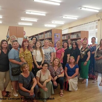 Grupa uśmiechniętych kobiet w bibliotece, w tle regały z ksiązkami.
