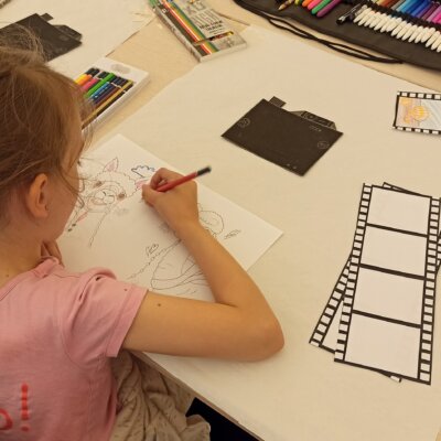 Dziewczynka siedzi przy stoliku i koloruje obrazek z alpaką