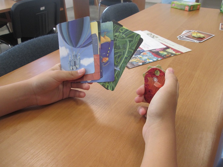 Karty "Dixit" w rękach grającego dziecka. Kliknięcie powoduje powiększenie zdjęcia
