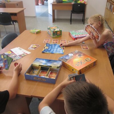 Dzieci grające w grę karcianą "Dixit" przy stole. Kliknięcie powoduje powiększenie zdjęcia