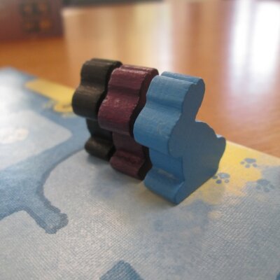 trzy drewniane króliczki w kolorach czarny, niebieski, fioletowy z gry karcianej "Dixit" stojące na planszy. Kliknięcie powoduje powiększenie zdjęcia