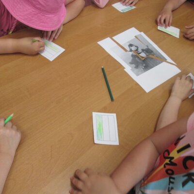 Dzieci kolorujące przy stole flagę na barwy Gorzowa Wielkopolskiego, obok Puzzle z pociętej kartki A4 z wizerunkiem maskotki Gorzowa Wielkopolskiego, Gorzusiem. Kliknięcie powoduje powiększenie zdjęcia