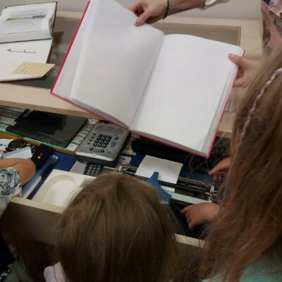 Pracownica Oddziału Integracji i Aktywności pokazuje książkę napisaną alfabetem Braillea. kliknięcie powoduje powiększenie zdjęcia