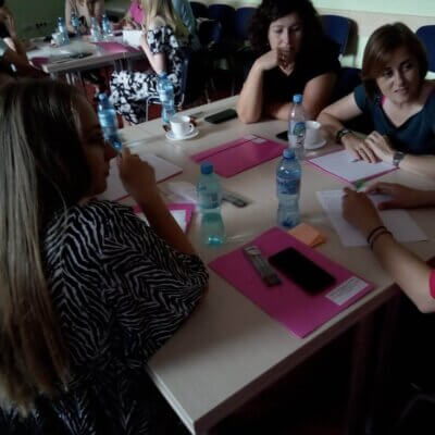 Kobiety siedzą przy stole z napojami i dokumentami. Wspólnie pracują nad zadaniem.