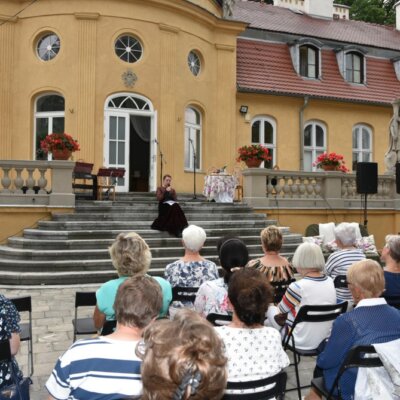 Aktorka siedzi na schodach przed Pałacem w Gliśnie i interpretuje poezję dwudziestoleci międzywojennego. Kliknięcie powoduje powiększenie zdjęcia