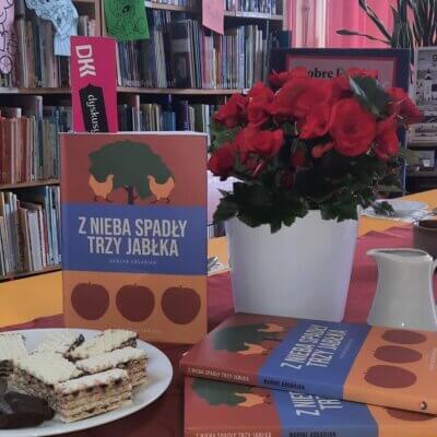 na stole obok kwiata w doniczce i ciastek na talerzu leżą trzy egz.omawianej ksiązki