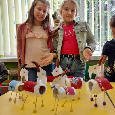 Dwie dziewczynki prezentują wykonane przez dzieci z papierowych rolek i patyczków koziłki poznańskie