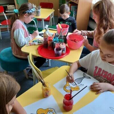 Dzieci siedzące przy stolikach malują wykonanymi przez siebie „rosnącymi farbami” postacie z warszawskich legend