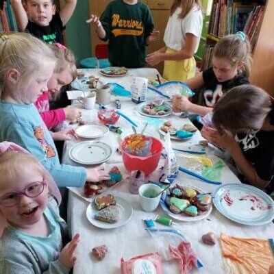 Dzieci siedzące przy stole ozdabiają pierniki kolorowym lukrem