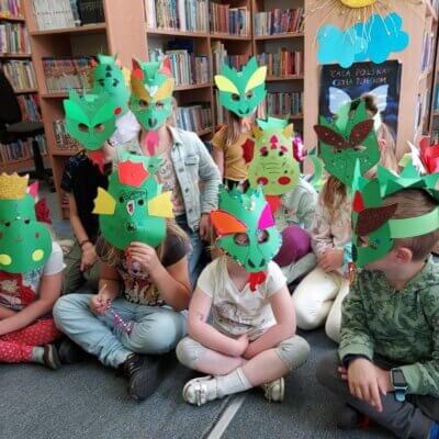 Grupa dzieci siedząca na dywanie w smoczych zielonych maskach
