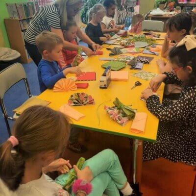 Dzieci siedzą przy stołach. Składają kolorowe serwetki