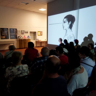 Goście oglądają wyświetlaną na ścianie prezentację z animacjami komputerowymi – dziełem autora prac. Kliknięcie powoduje powiększenie zdjęcia.