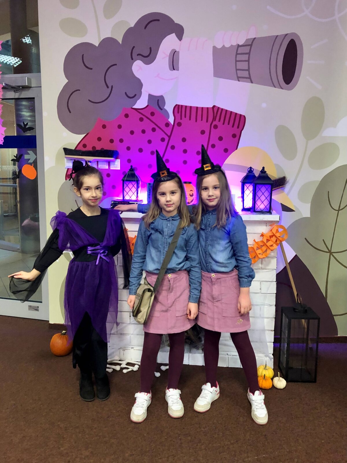Trzy dziewczynki przebrane za czarownice pozują do wspólnego zdjęcia na tle halloweenowego kominka.