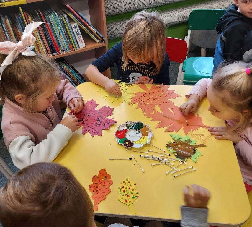 Dzieci siedzące przy stoliku nadają jesienne kolory za pomocą patyczków higienicznych i farb liściom wyciętym z papieru
