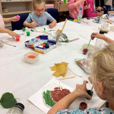 Dziewczynki w skupieniu malują farbami wykonane własnoręcznie gliniane listki. Kliknięcie powoduje powiększenie zdjęcia.
