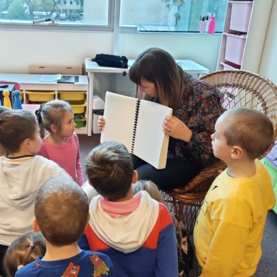 2. Pani Bibliotekarka prezentuje dzieciom książkę napisaną alfabetem Braille'a. Dzieci uważnie przyglądają się strukturze stron. Kliknięcie powoduje powiększenie zdjęcia.