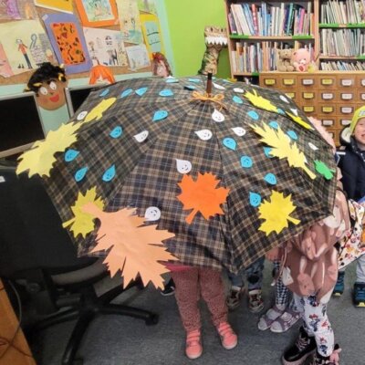 Dzieci ukryte pod parasolem, który ozdobiły wyciętymi z papieru uśmiechniętymi kropelkami deszczu i kolorowymi jesiennymi listkami. Klikniecie powoduje powiększenie zdjęcia.