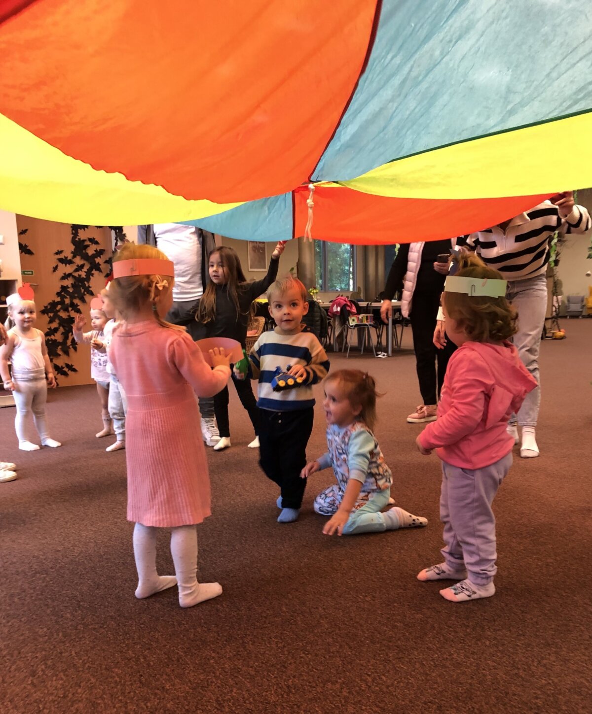 Dzieci w kolorowych opaskach stoją pod chustą animacyjną.