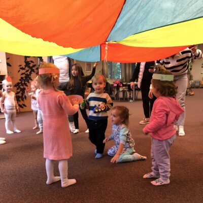 Dzieci w kolorowych opaskach stoją pod chustą animacyjną.